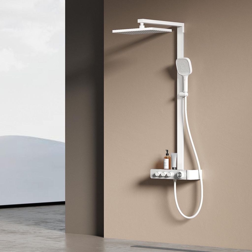 A modern white shower system mounted on a beige wall, with a glimpse of a minimalist outdoor scene in the background.
