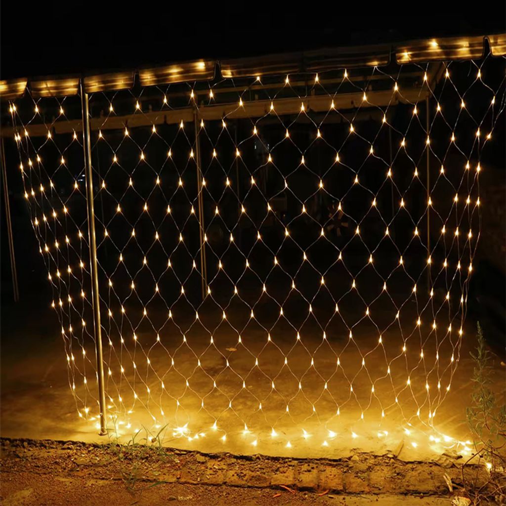 A net of warm white LED lights is hung outdoors at night, illuminating the ground below.