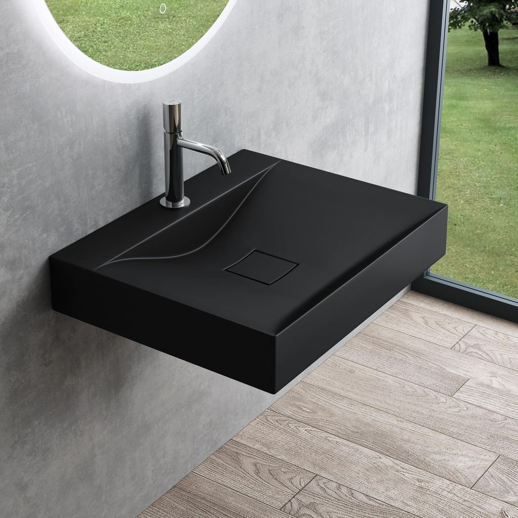 A modern black matte washbasin mounted on a gray wall, with a large window showing a green outdoor landscape in the background.