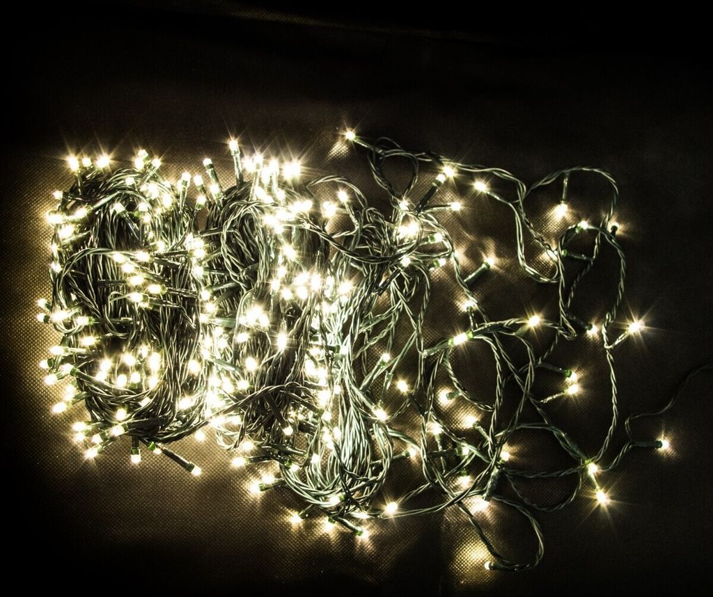 A tangled pile of white LED string lights with green wire on a dark background.