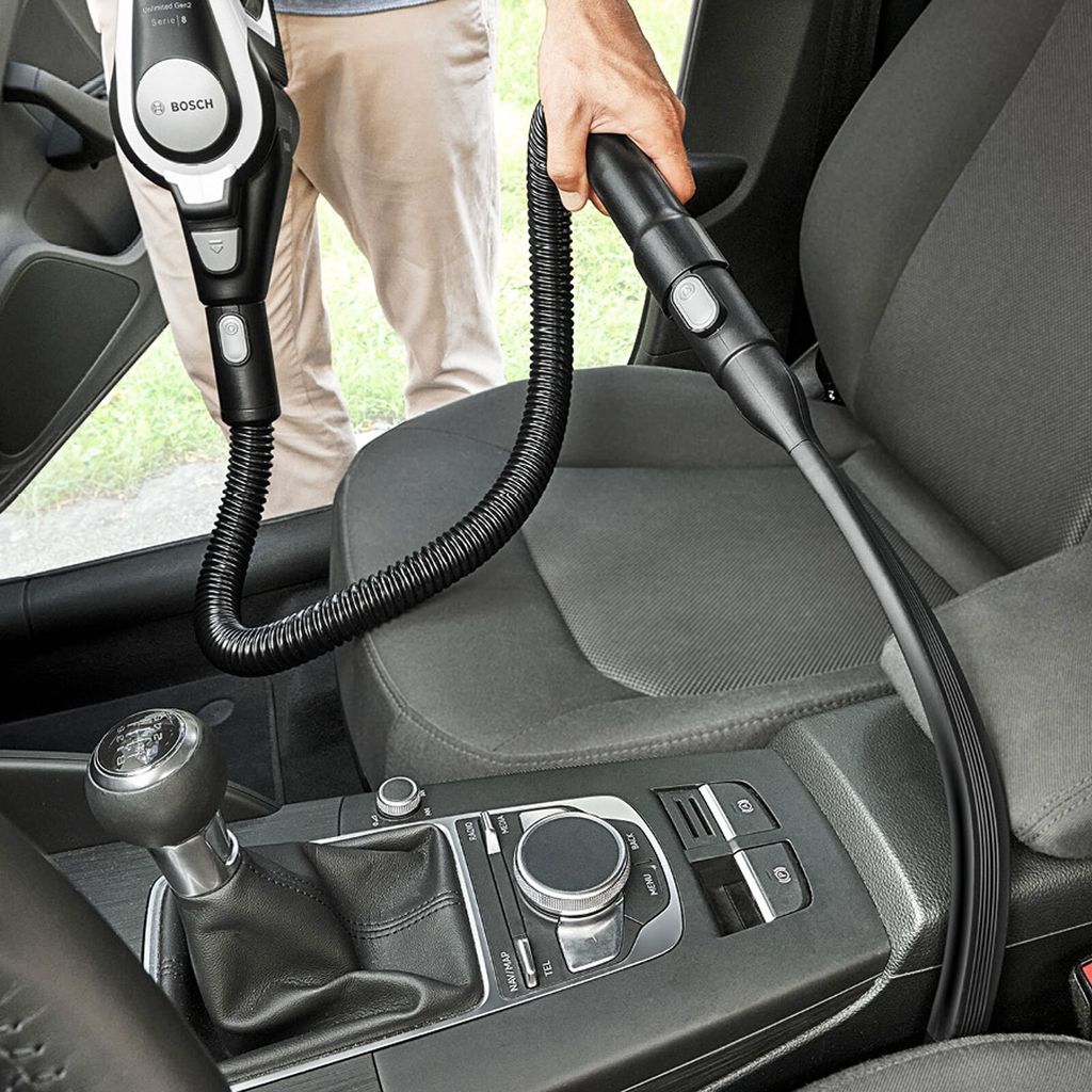 A person is vacuuming the interior of a car with a Bosch handheld vacuum cleaner.