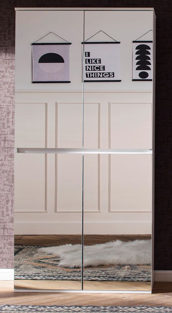 A tall, white wardrobe with mirrored doors, decorated with three framed posters at the top. The floor and a rug are reflected in the mirrored doors.