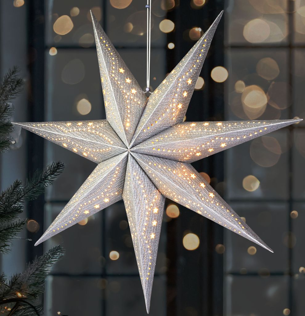 A silver 3D paper star with small lights is hanging in front of a window with bokeh lights.