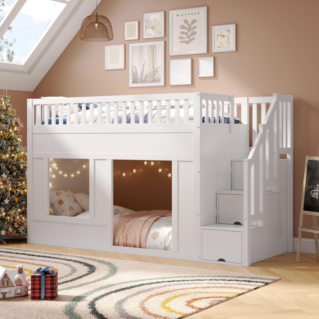 A white bunk bed with stairs is set up in a room with a Christmas tree and artwork on the wall.