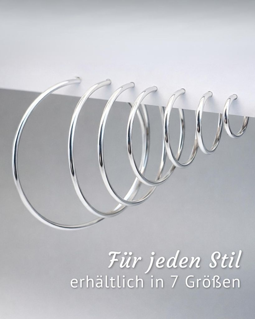 7 silberne Creolen in verschiedenen Größen hängen nebeneinander an einem weißen Display - minimalistisches Design. Unten rechts steht der Text 'Für jeden Stil - erhältlich in 7 Größen'