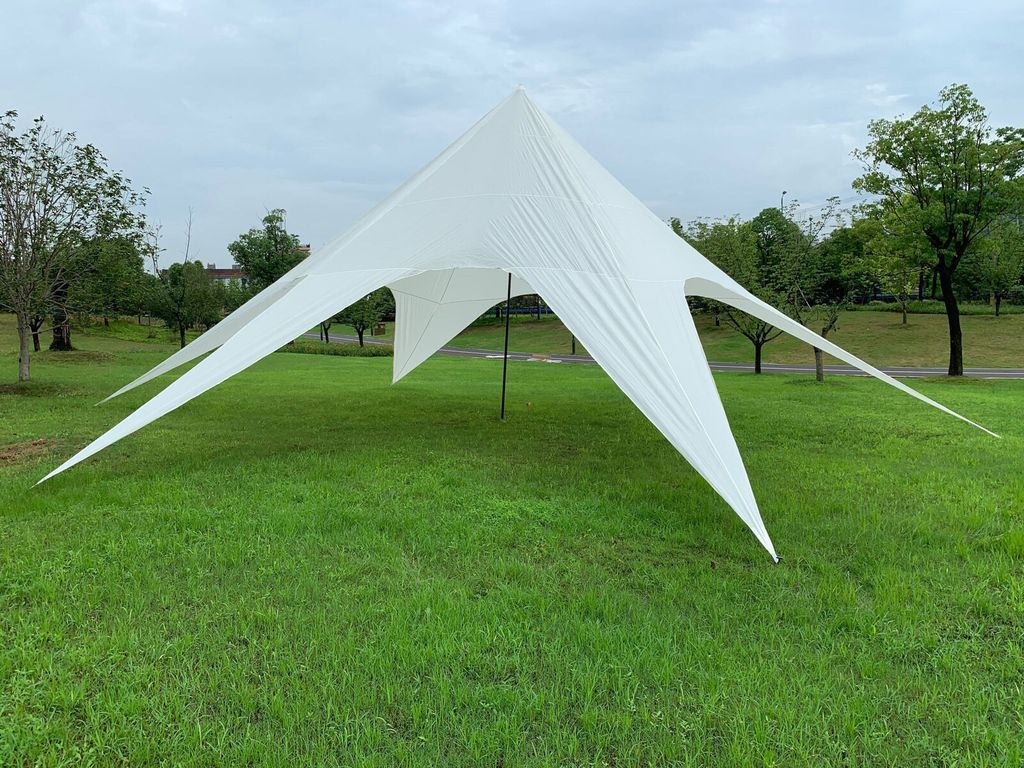 A white star-shaped tent is set up on a grassy field with trees in the background.
