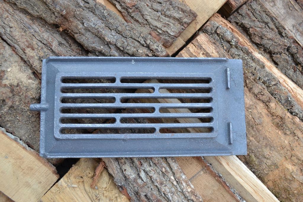 A cast iron stove grate is placed on a pile of firewood.