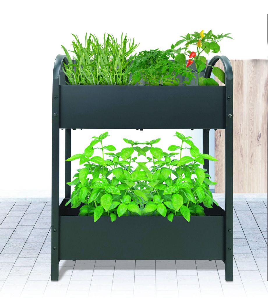 A two-tiered black planter box with various green plants growing in it, placed on a tiled floor.