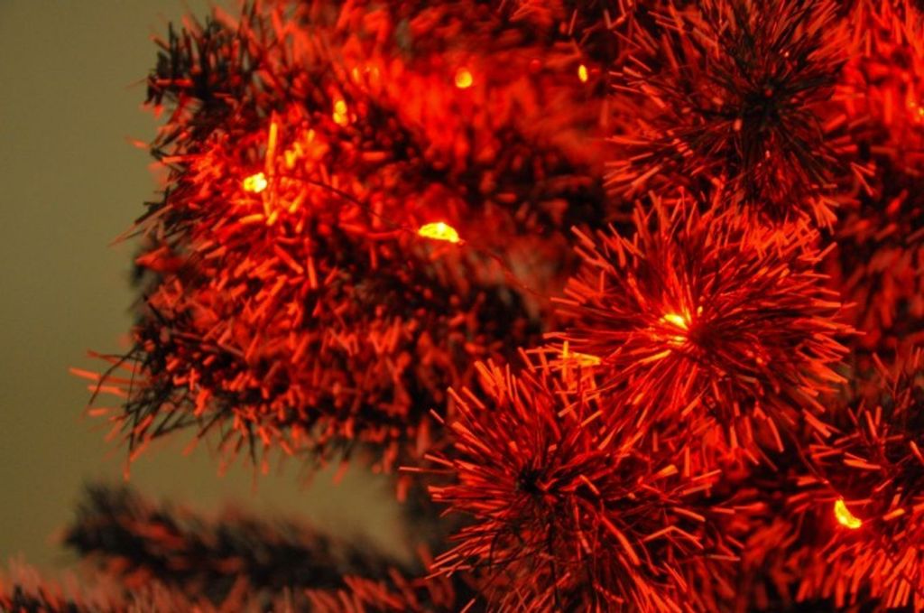 A close-up view of red Christmas tree tinsel with small orange lights.