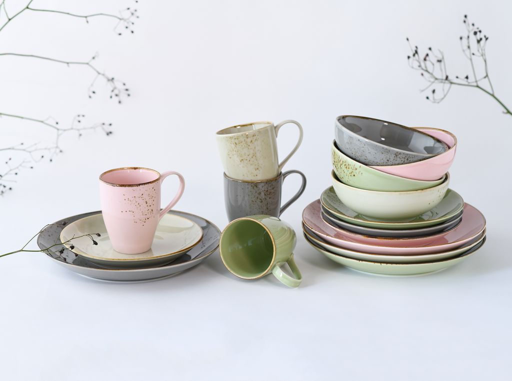 A collection of ceramic tableware, including mugs and plates, arranged on a white surface with decorative branches in the background.