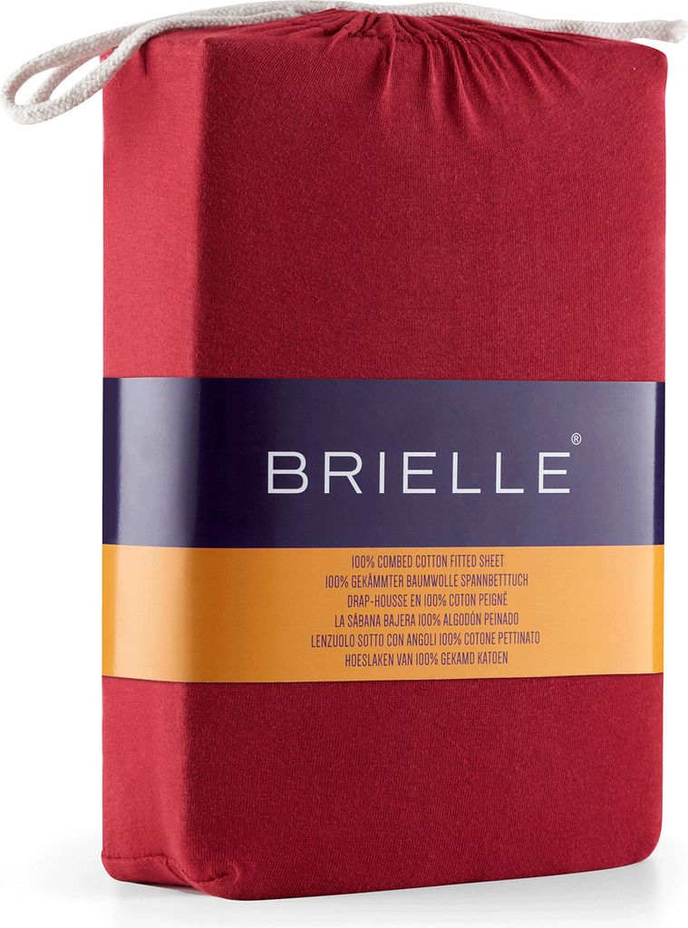 A folded red fitted sheet packaged in its own fabric bag, with a branded label wrapped around it.