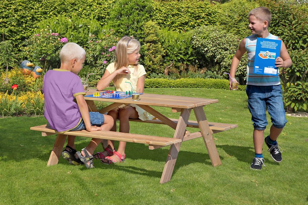Three children are playing and sitting around a wooden picnic table in a garden.