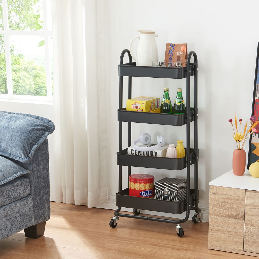 A black four-tier rolling cart filled with various items, placed next to a sofa and a window with white curtains.