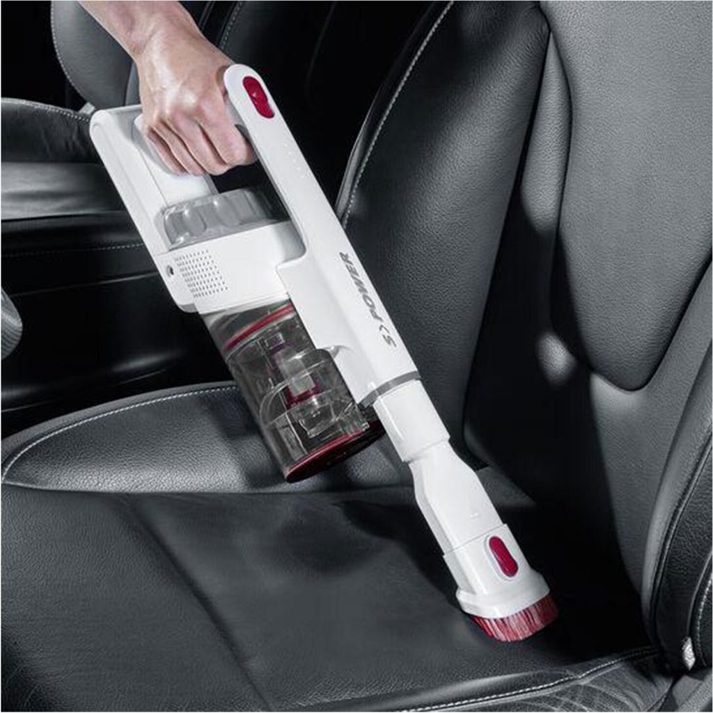 A hand holding a white and red cordless vacuum cleaner on a black car seat.