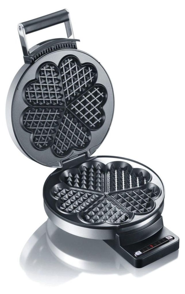 An open waffle iron with heart-shaped molds.