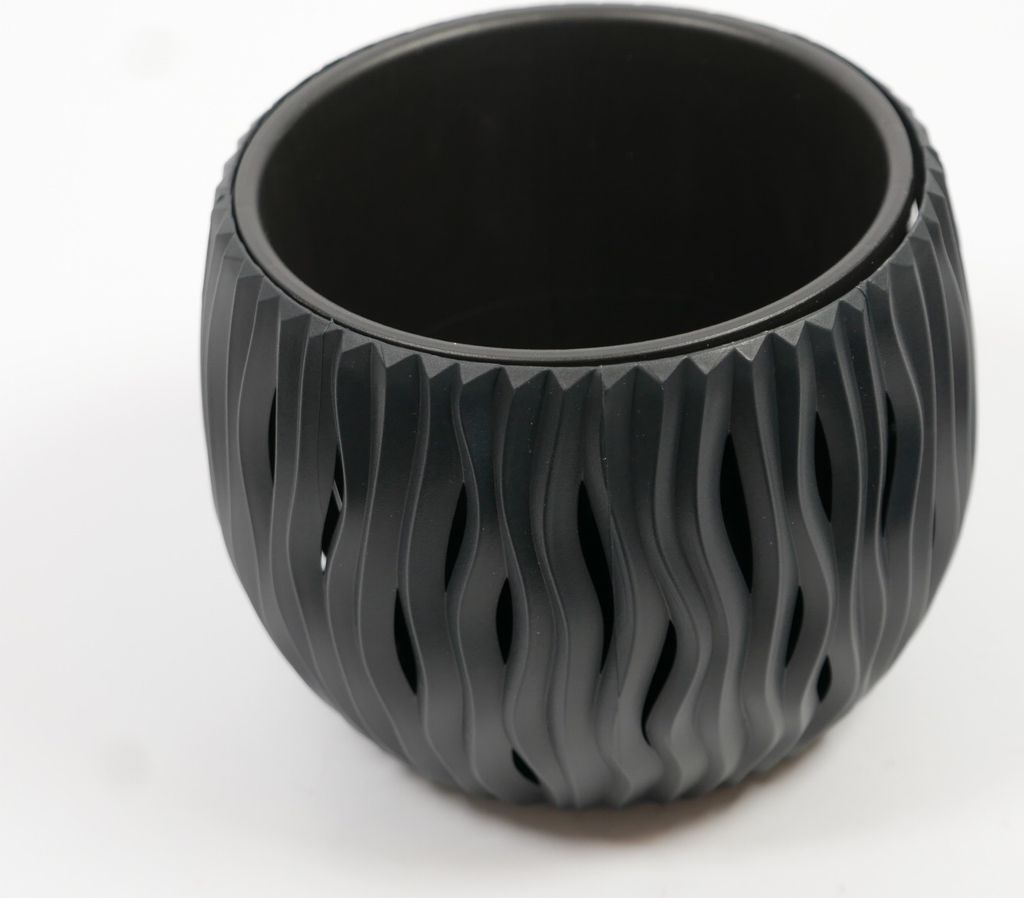 A black planter with a wavy, cut-out design sits on a white surface.