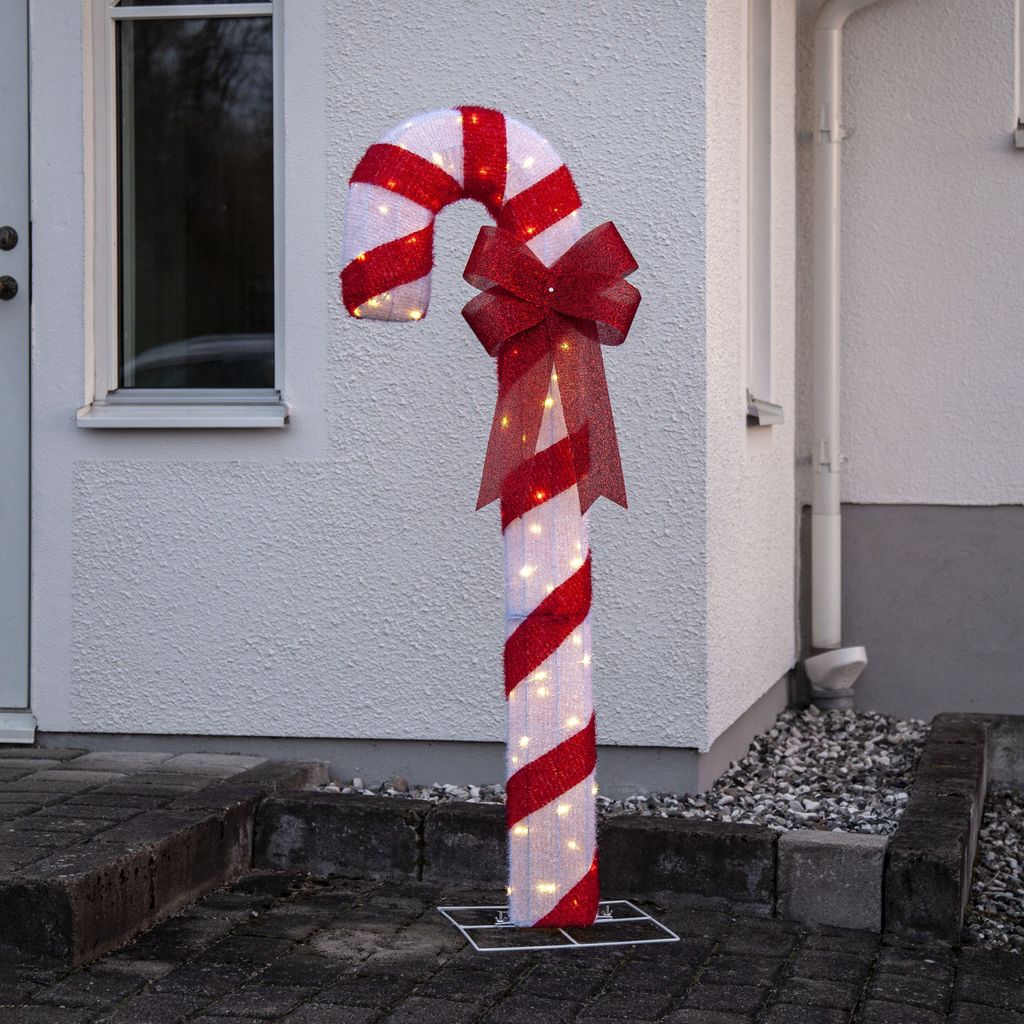 A lighted candy cane decoration stands outside a house.