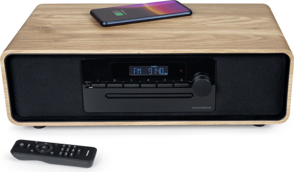 A Thomson Micro-Kompaktanlage MIC300IBT sits on a white surface with a remote control in front of it and a smartphone on top.