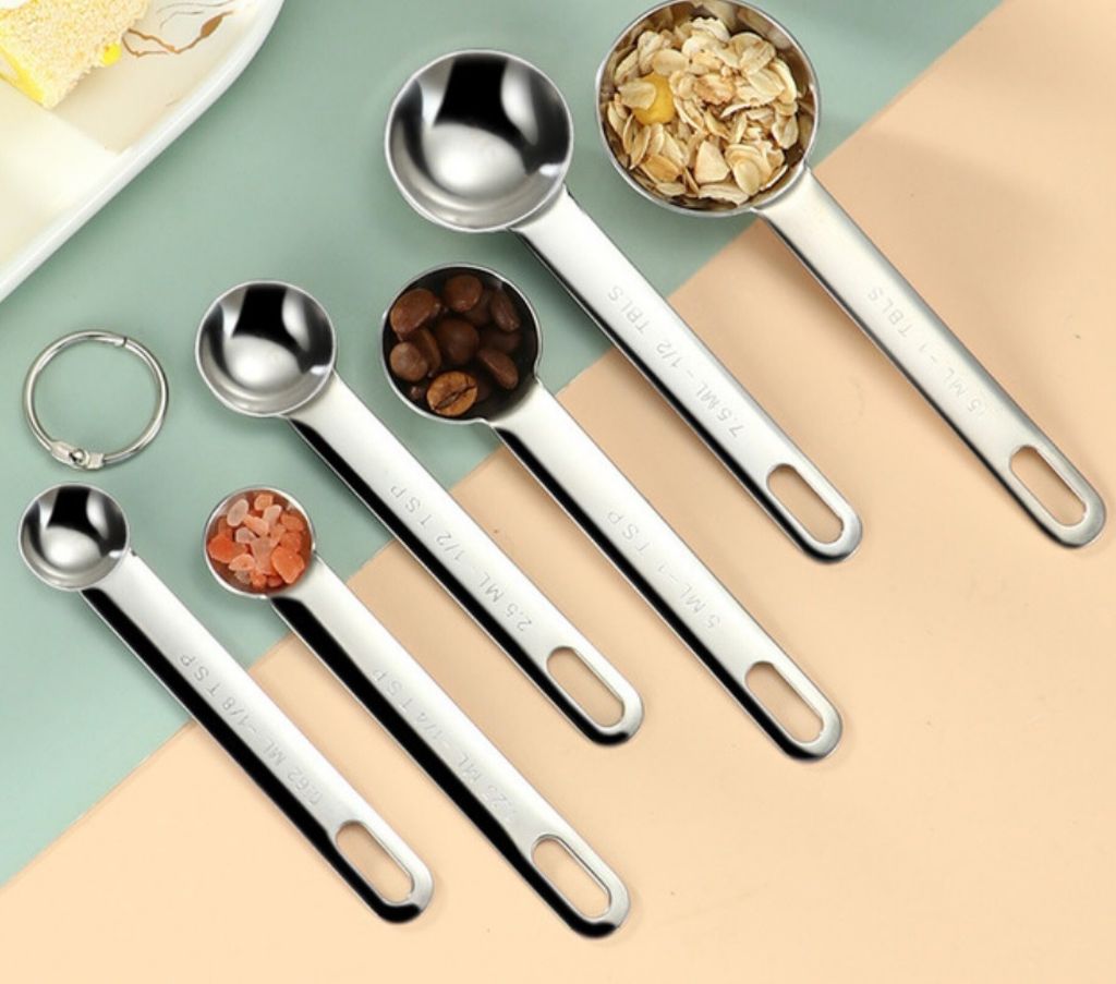 A set of stainless steel measuring spoons arranged diagonally on a light green and peach background.