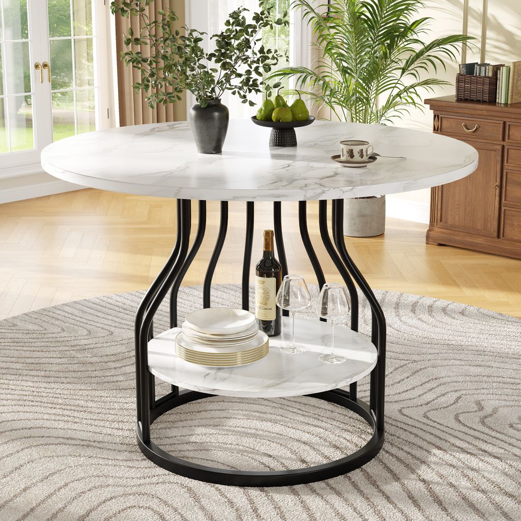 A round dining table with a marble-like top and black metal legs, set in a dining room with plants and furniture in the background.