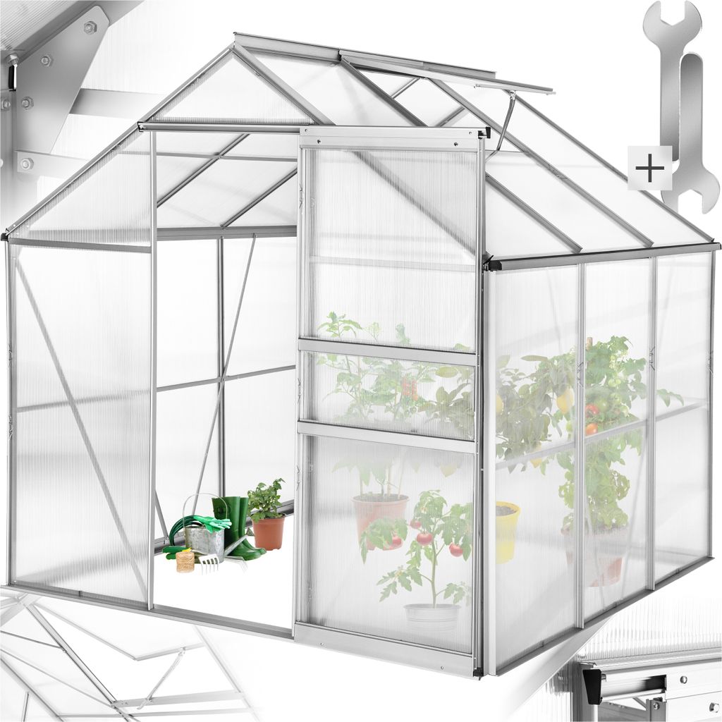 A greenhouse with plants inside, showing gardening tools near the entrance.