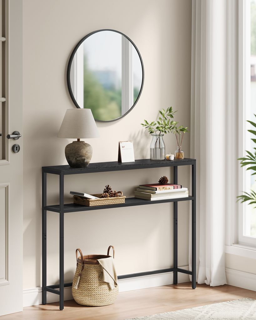 A narrow console table with two shelves, decorated with a lamp, books, and a basket, placed in a hallway next to a door and window.
