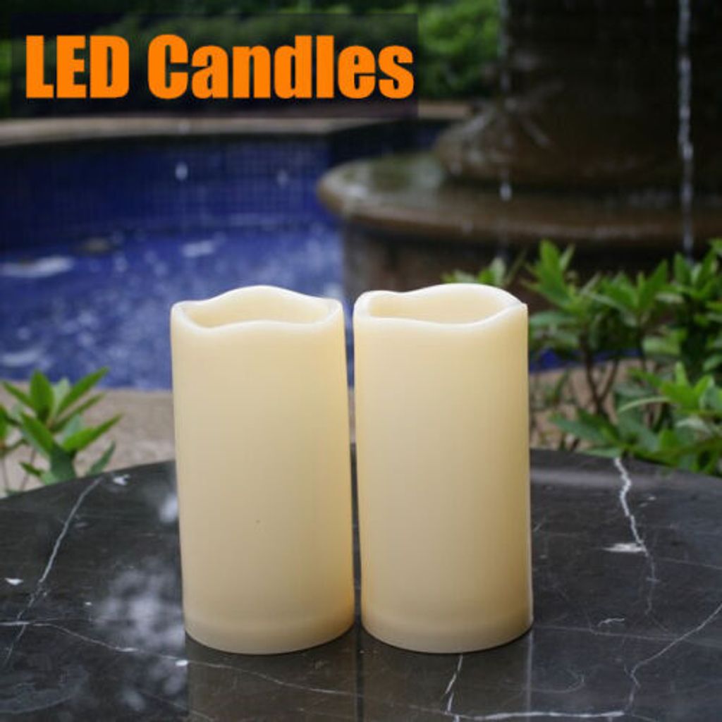 Two LED candles are placed on a marble table in front of a fountain and pool.