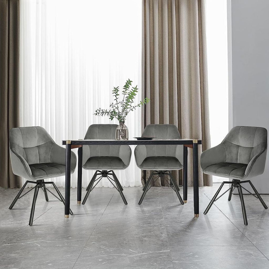 Four gray velvet dining chairs arranged around a dark wooden dining table with a vase of greenery and a plate on top.