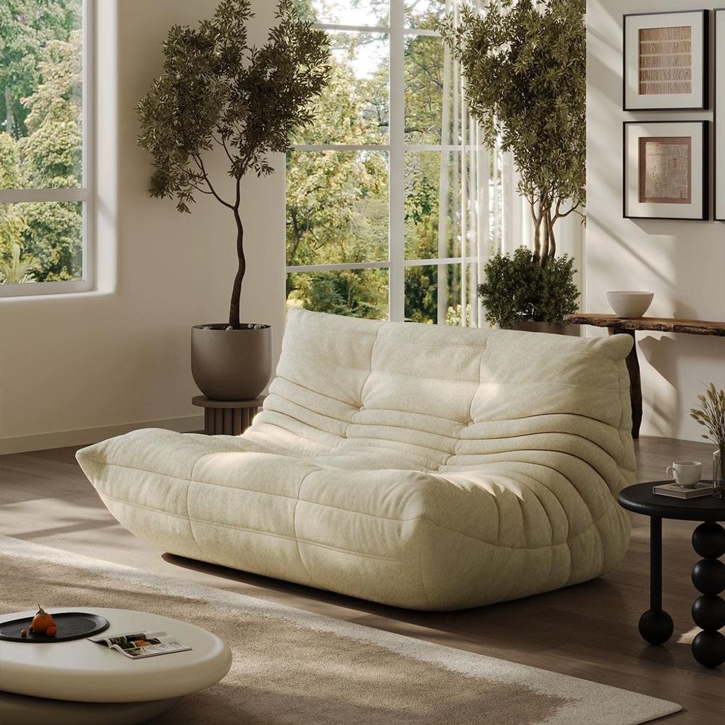 A modern living room with a beige sofa, large windows, and plants.
