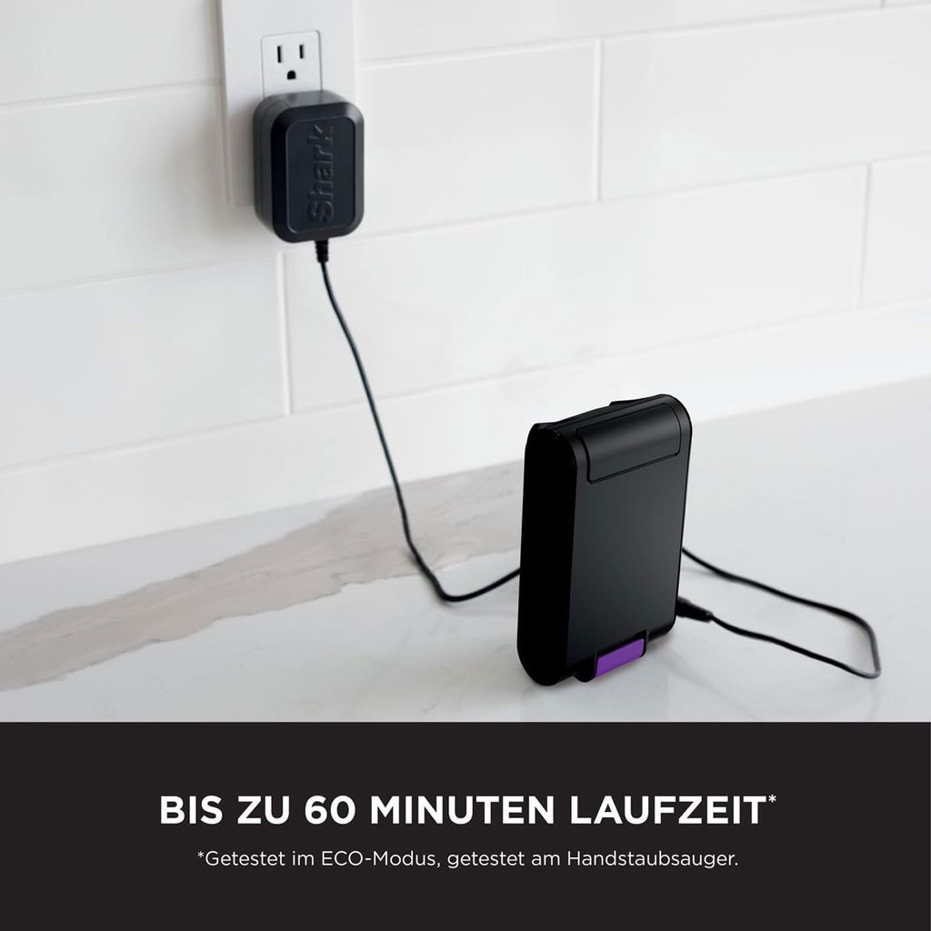 A black Shark brand charger plugged into a white wall outlet, connected by a black cord to a black battery pack with a purple accent, resting on a white countertop.