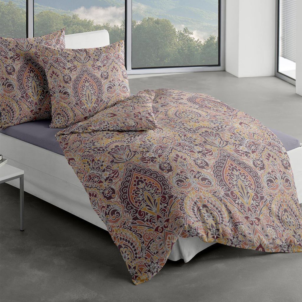 A bed with patterned bedding and pillows in a room with a large window overlooking a landscape.