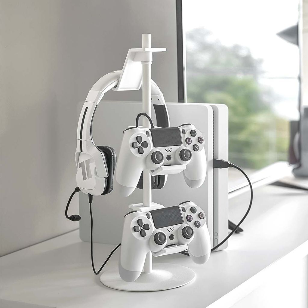 A white gaming accessory stand holding headphones and two controllers, with a white gaming console in the background.