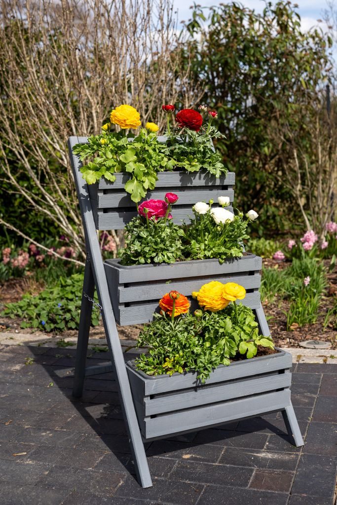 A tiered planter filled with colorful flowers on a paved patio.