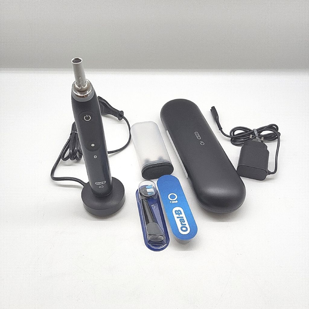 A black Oral-B iO electric toothbrush and its accessories are laid out on a white surface.