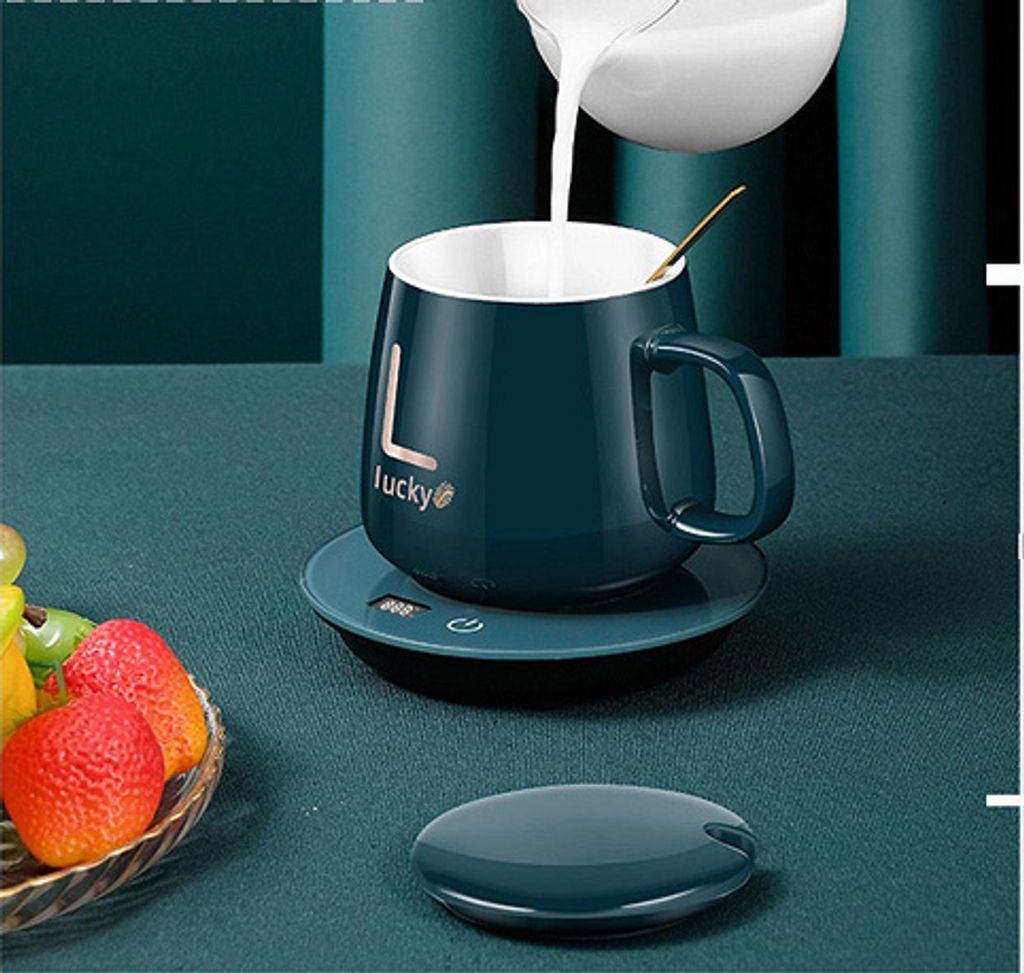 A dark teal mug with the word 'Lucky' on it is being filled with milk, sitting on a matching coaster. A small dish of strawberries is in the foreground.