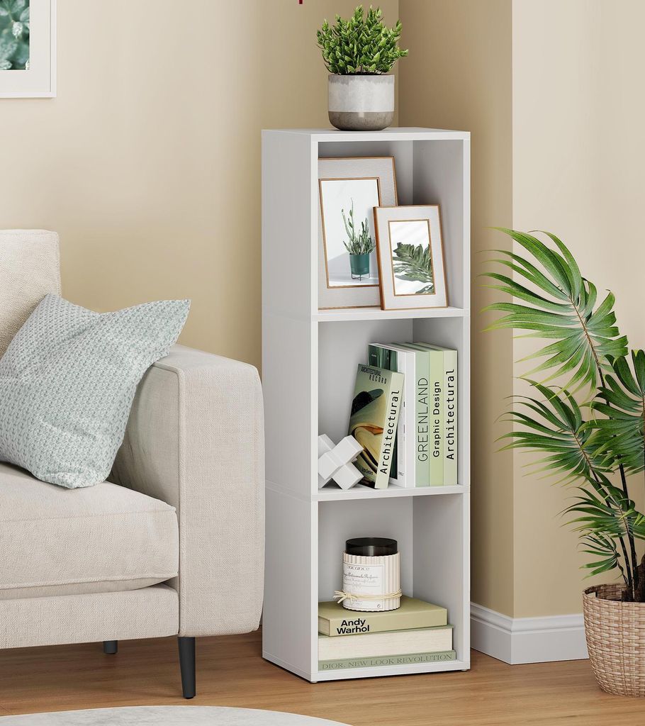 A white, three-tiered bookshelf placed next to a couch and a large potted plant.