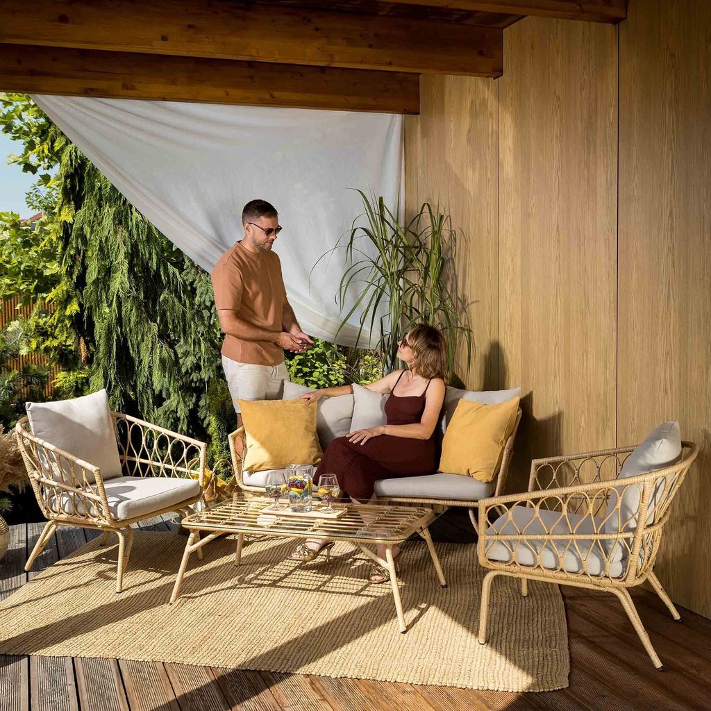 A couple is relaxing on a patio set on a wooden deck, surrounded by greenery.