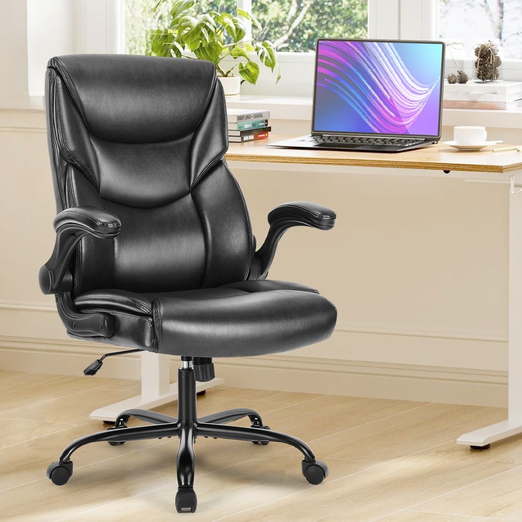 A black office chair is shown in a home office setting with a desk and laptop in the background.