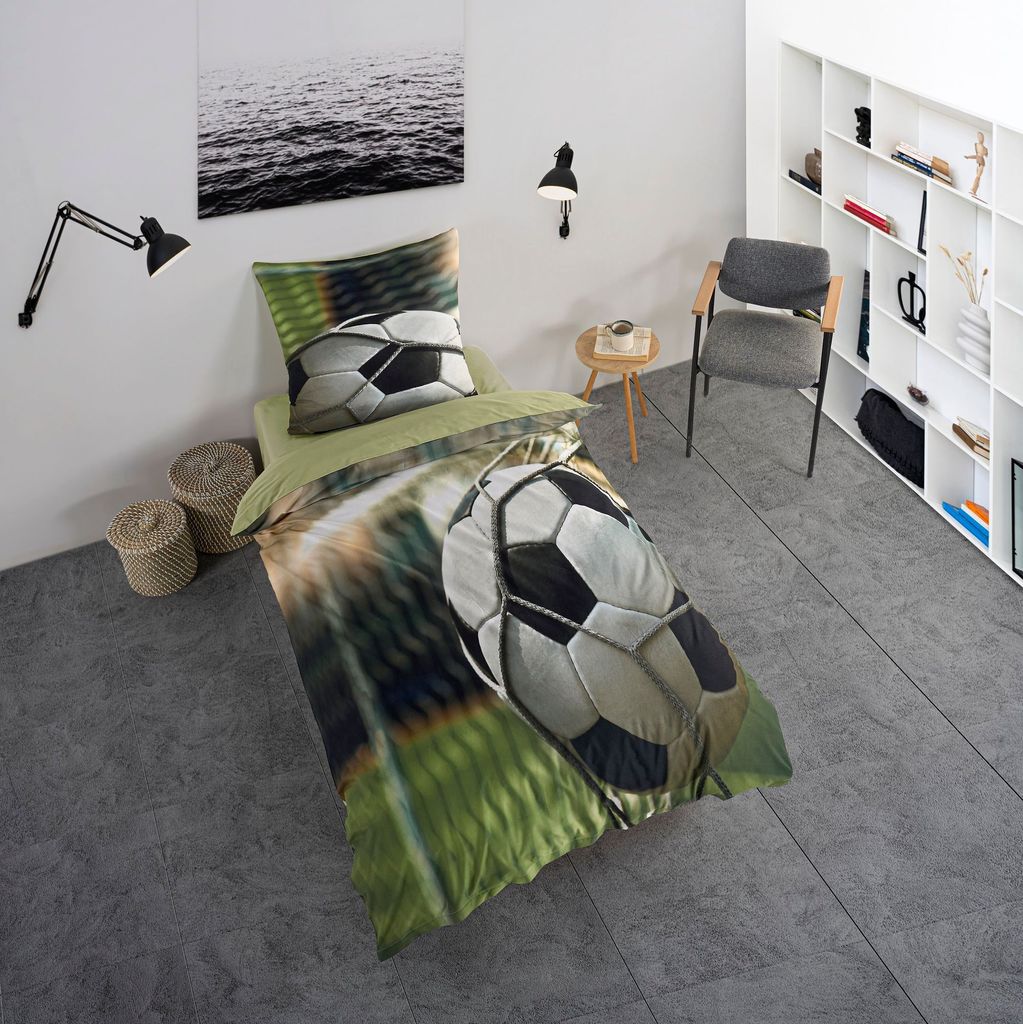 A bedroom scene with a bed featuring football-themed bedding, a chair, and a bookshelf.