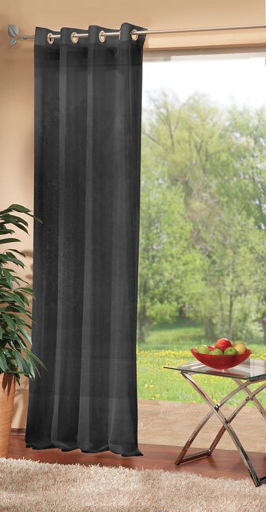 A dark grey curtain hangs in front of a large window with a view of a garden. A small glass table with a bowl of fruit sits to the right of the curtain.