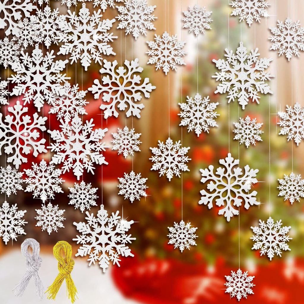 Hanging white snowflakes with a blurred Christmas tree in the background.