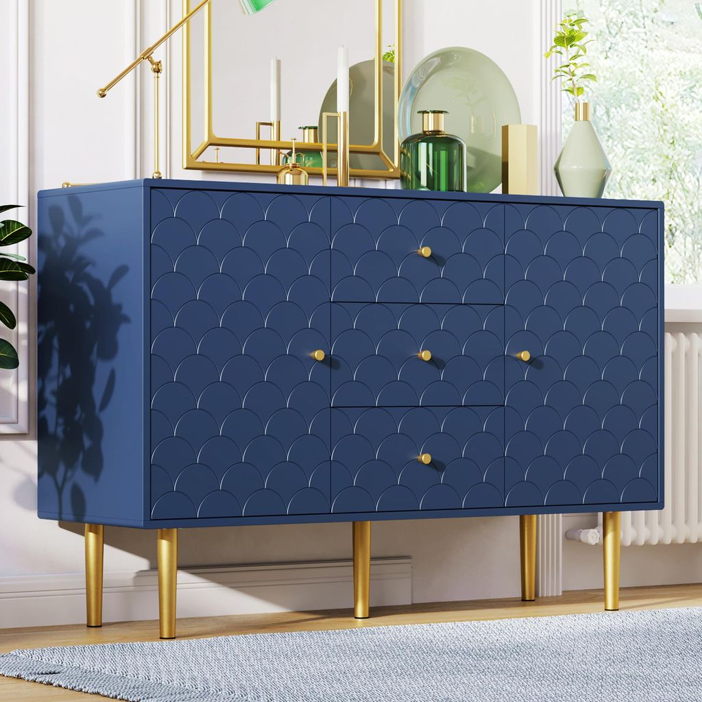 A navy blue dresser with gold legs and gold drawer pulls, decorated with a scalloped pattern. It is placed on a light blue rug in a well-lit room.