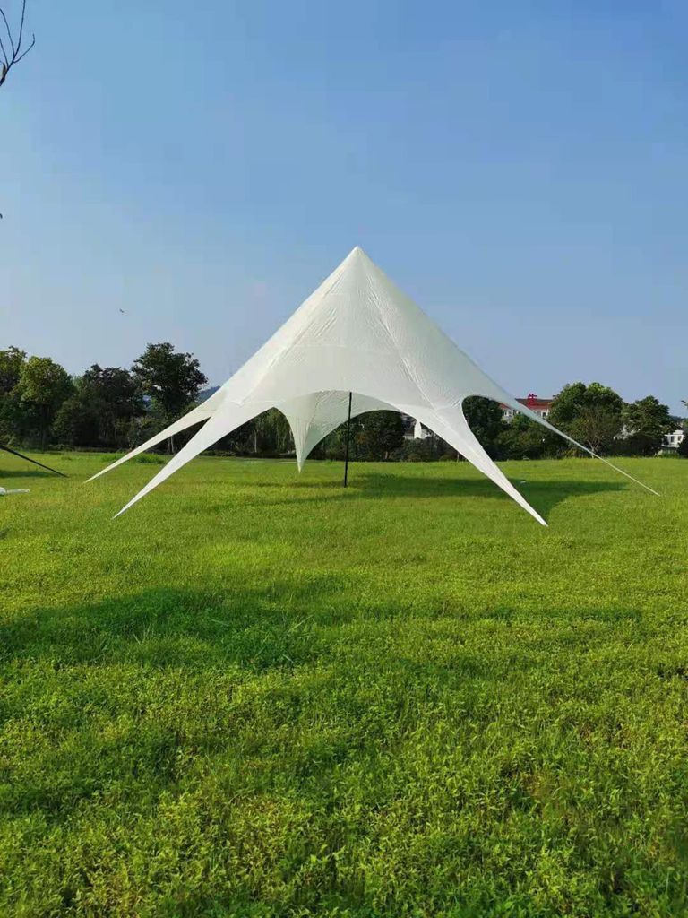 A white star tent is set up on a green grassy field under a clear blue sky.
