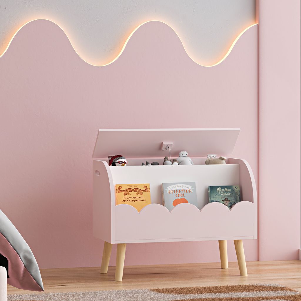 A pink toy chest with books and toys inside, placed in a child's room with a pink wall and a wavy light fixture.