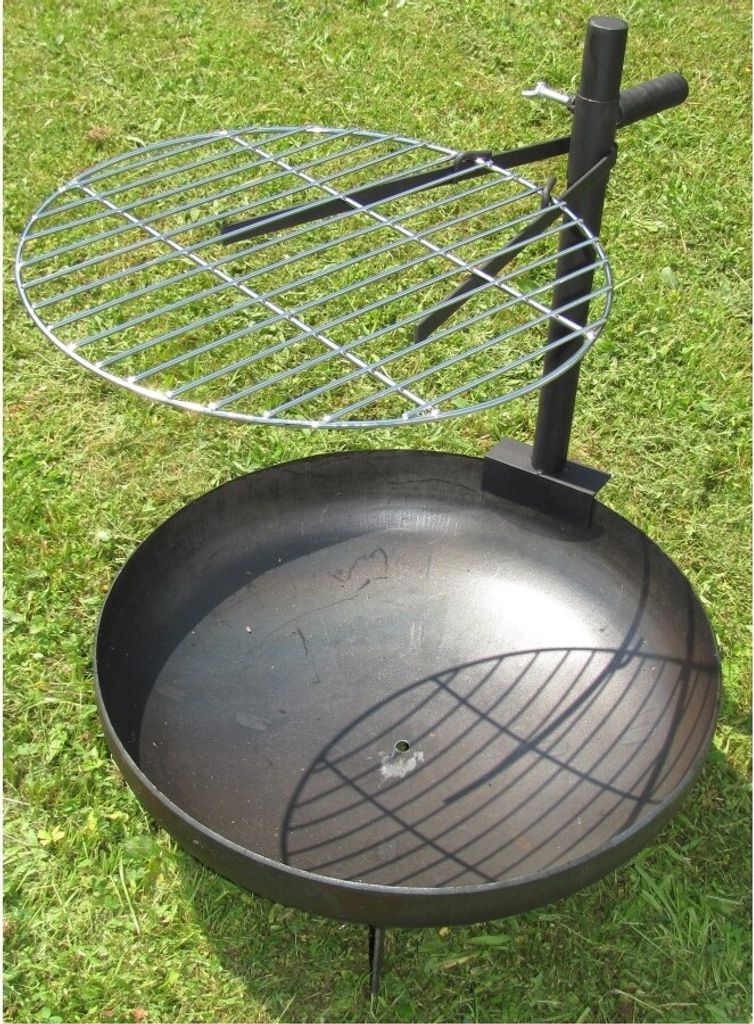A metal fire pit with a grill grate on a grassy lawn.