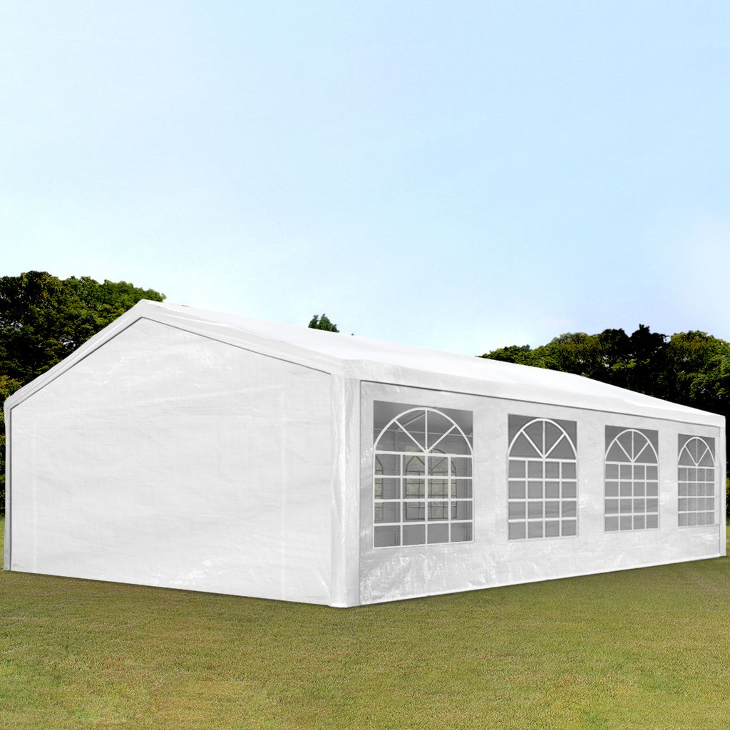 A white party tent with arched windows is set up on a grassy lawn with trees and a blue sky in the background.