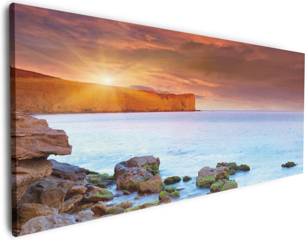 Wallario Premium Leinwandbild Sonnenaufgang am Meer mit Landzunge und Felsen im Wasser in Größe 50 x 125 cm