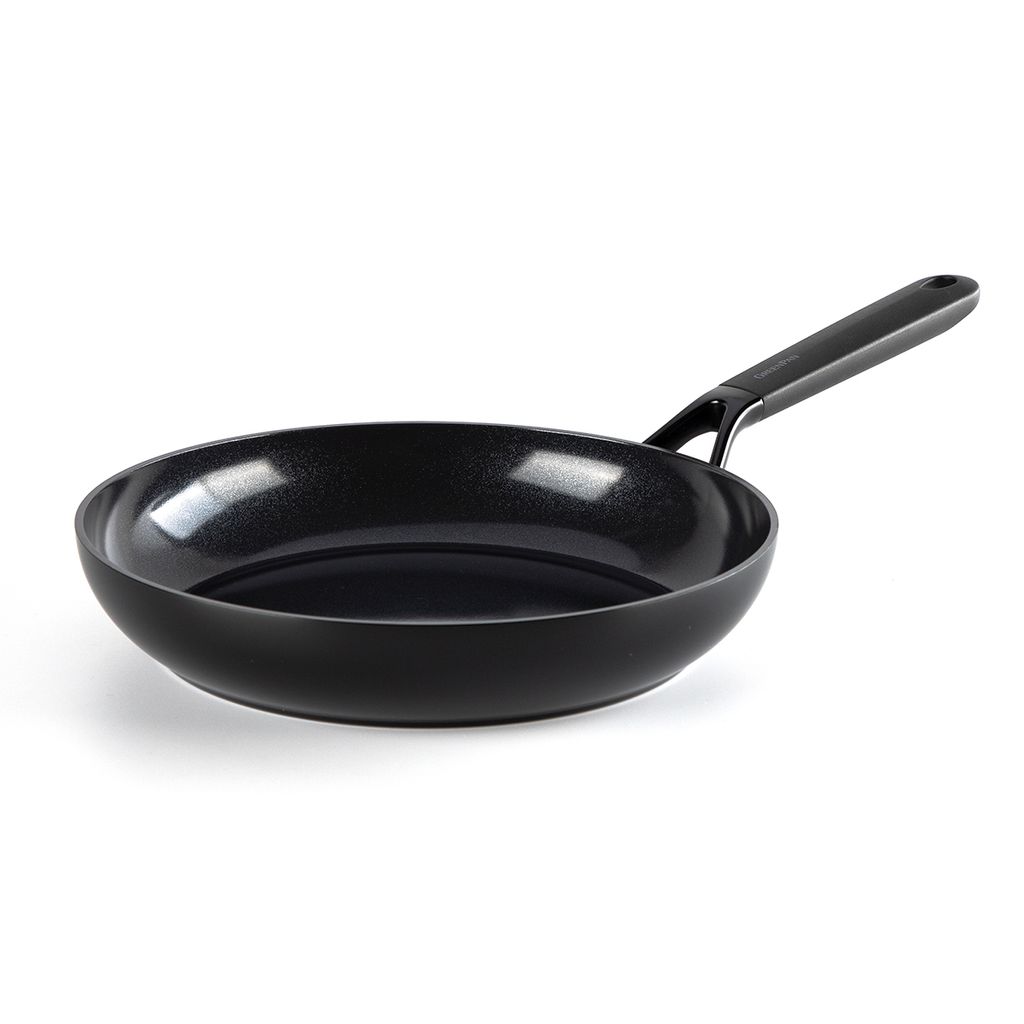 A black frying pan with a speckled interior and a black handle is shown against a white background.