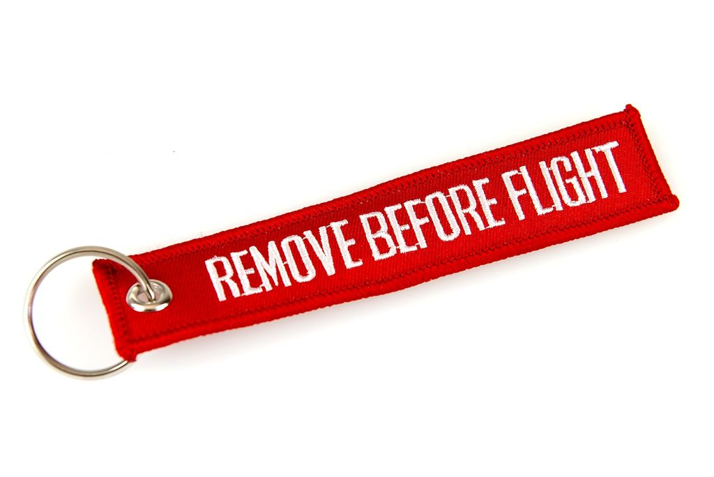 A red keychain with white text that says "REMOVE BEFORE FLIGHT" and a silver ring, isolated on a white background.