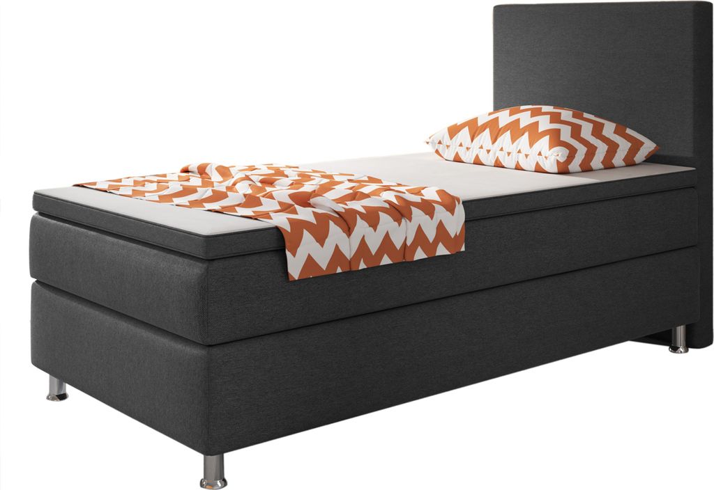 A single bed with a dark grey base and headboard, a white mattress, and a patterned throw blanket and pillow in orange and white.